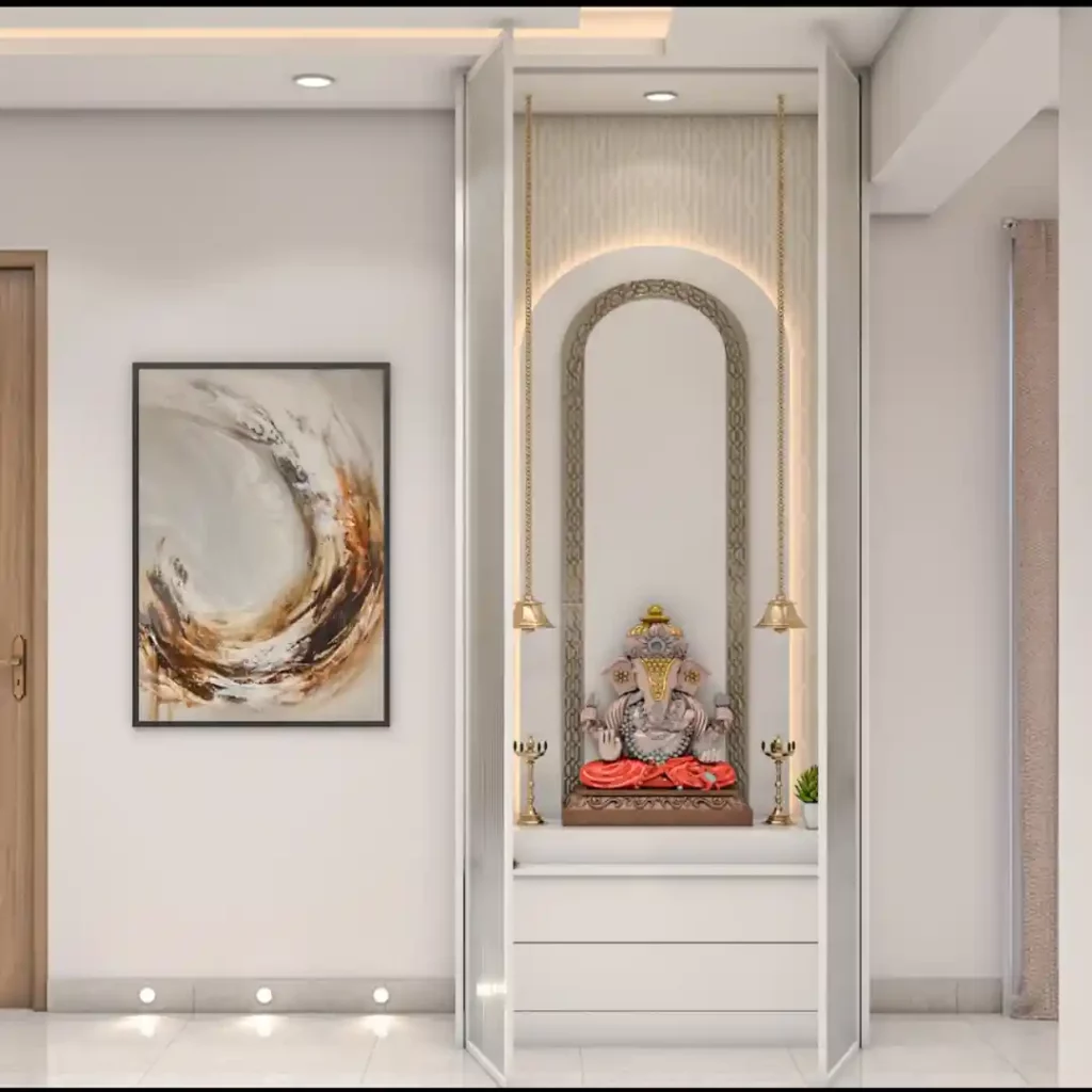 Modern pooja niche with Ganesha idol, arched design, LED lighting, and golden bells — elegant minimalist prayer space in white