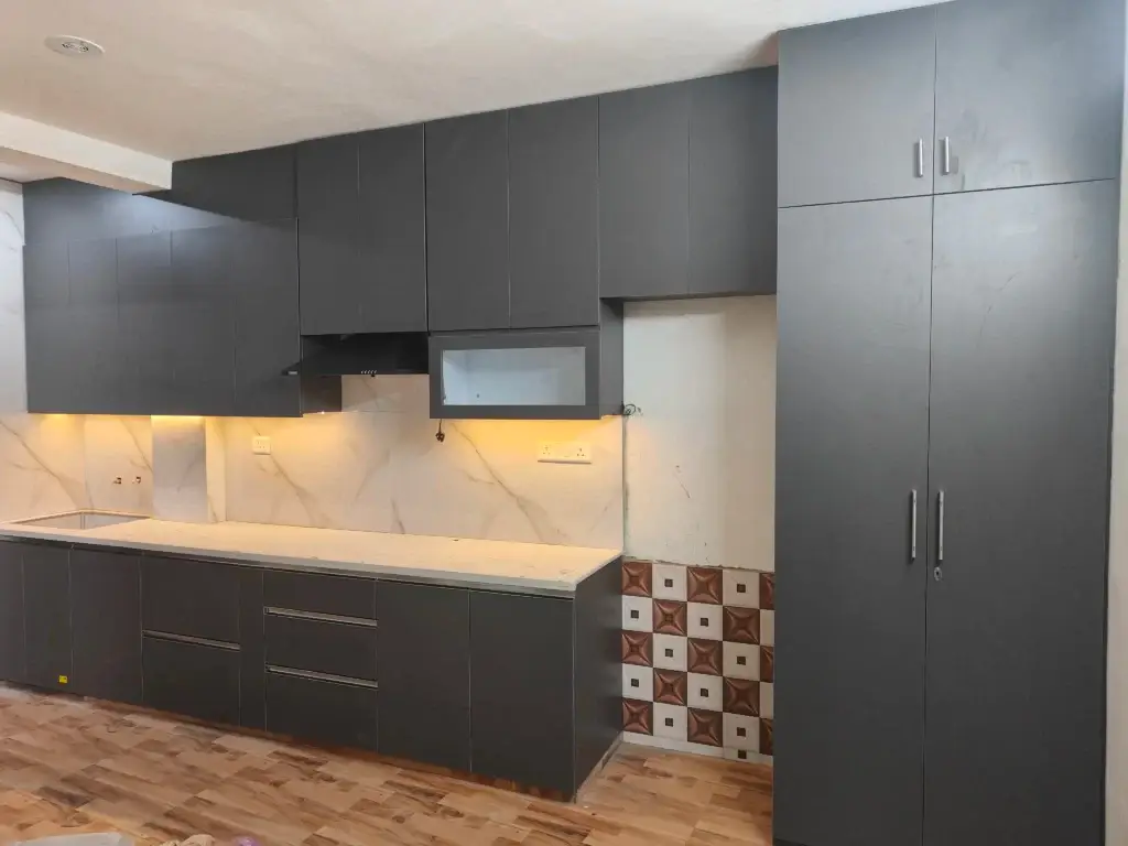 Modern kitchen with sleek black cabinets, white marble backsplash, and wooden flooring, ideal for homes in Delhi, Gurgaon, and Noida.